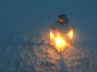 Laterne im Schnee Zu sehen ist eine Laterne in der eine Kerze brennt. Die Laterne steht auf dem verschneiten Boden.